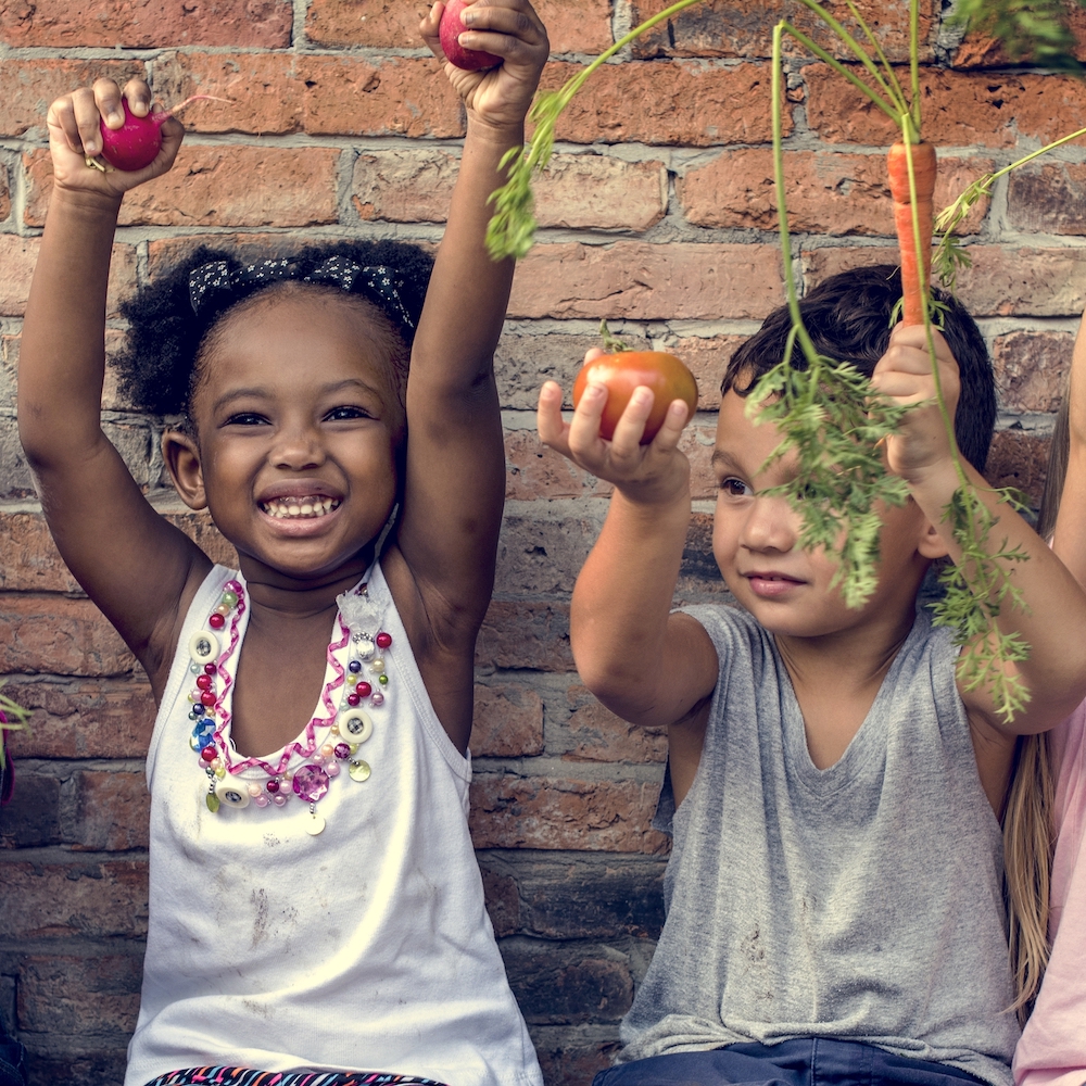 Two children holding up vegetables from a garden